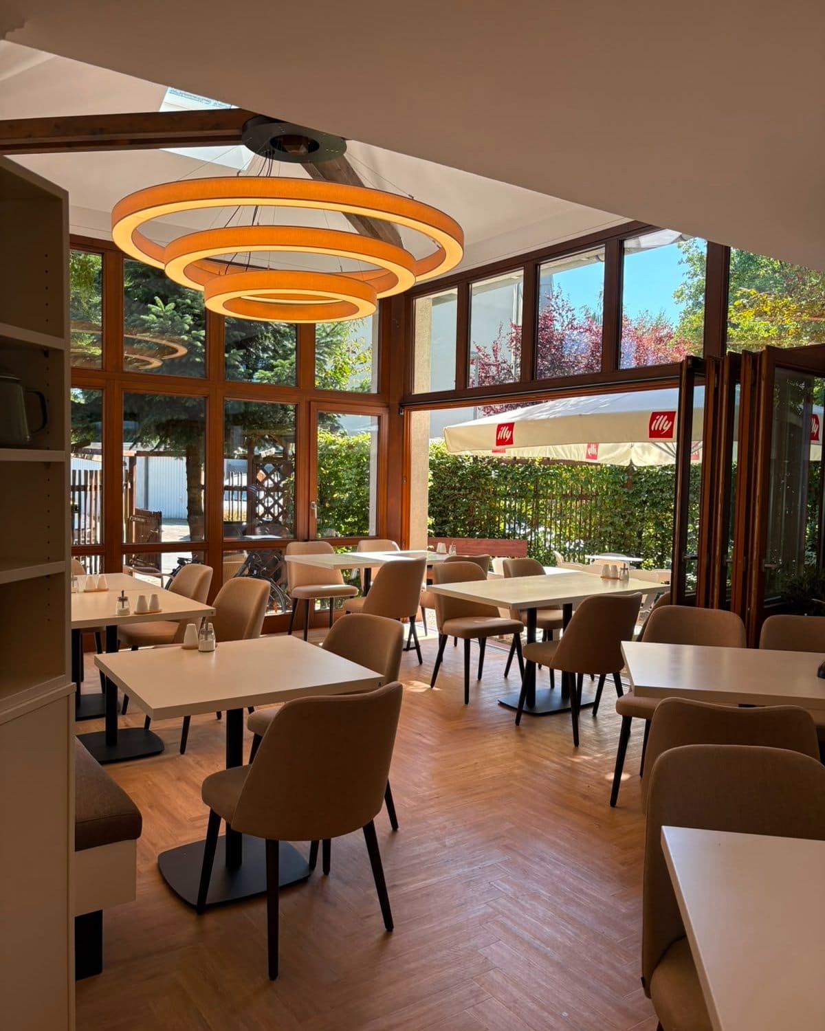Heller Wintergarten des Café Ava mit Tischen, Polsterstühlen und großen Holzfenstern