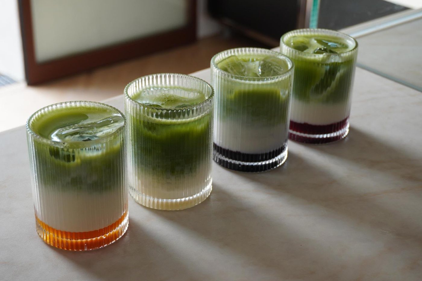 Vier Gläser Matcha Latte mit Fruchtsirup auf einer Marmorplatte