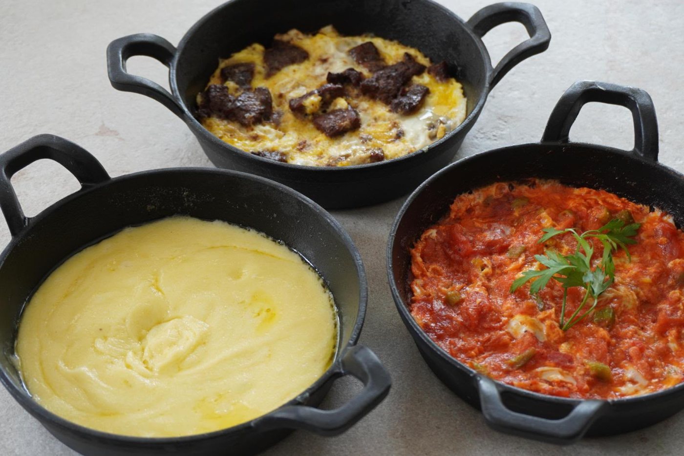 Drei gusseiserne Pfannen mit Sucuklu Yumurta, Kuymak und Menemen