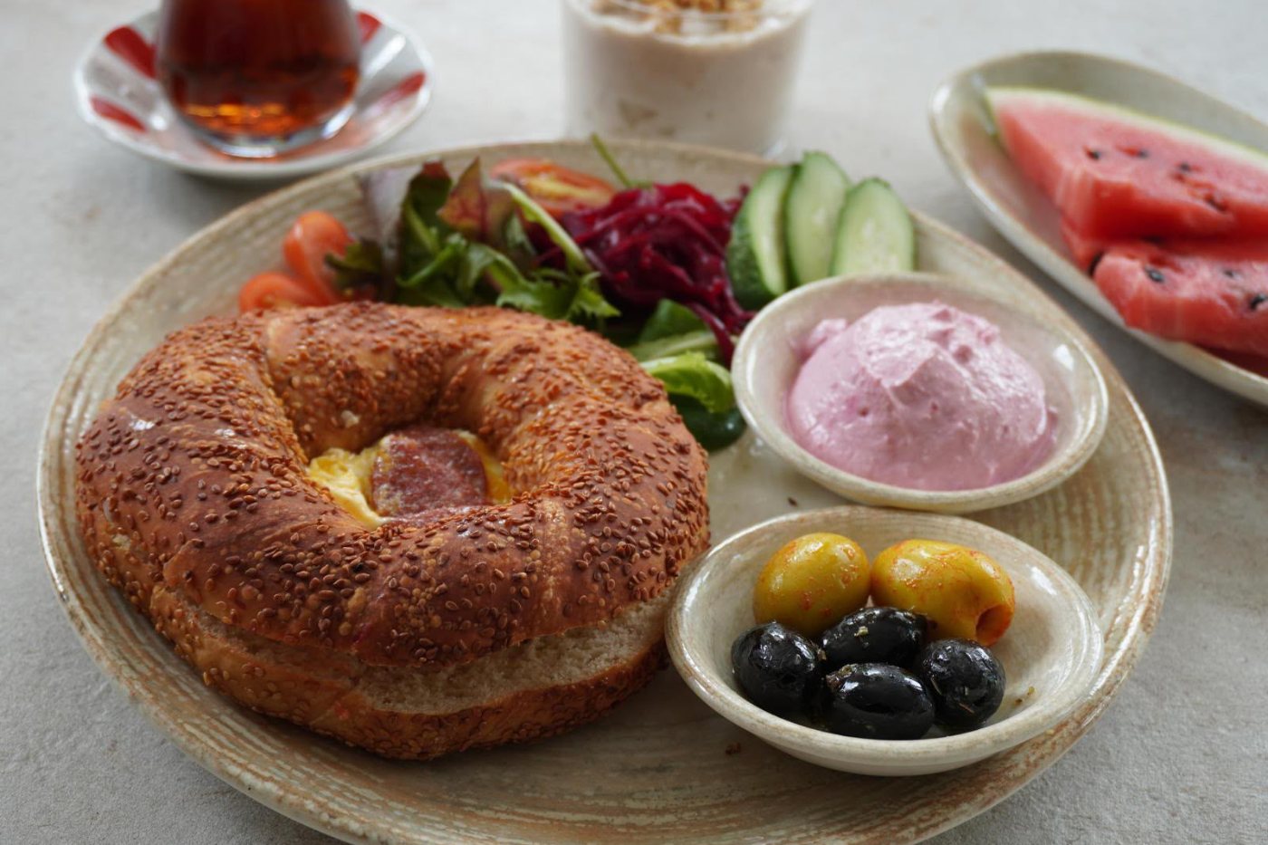 Gefüllter Simit mit Salat, Joghurt, Oliven, Wassermelone und einem Glas Çay